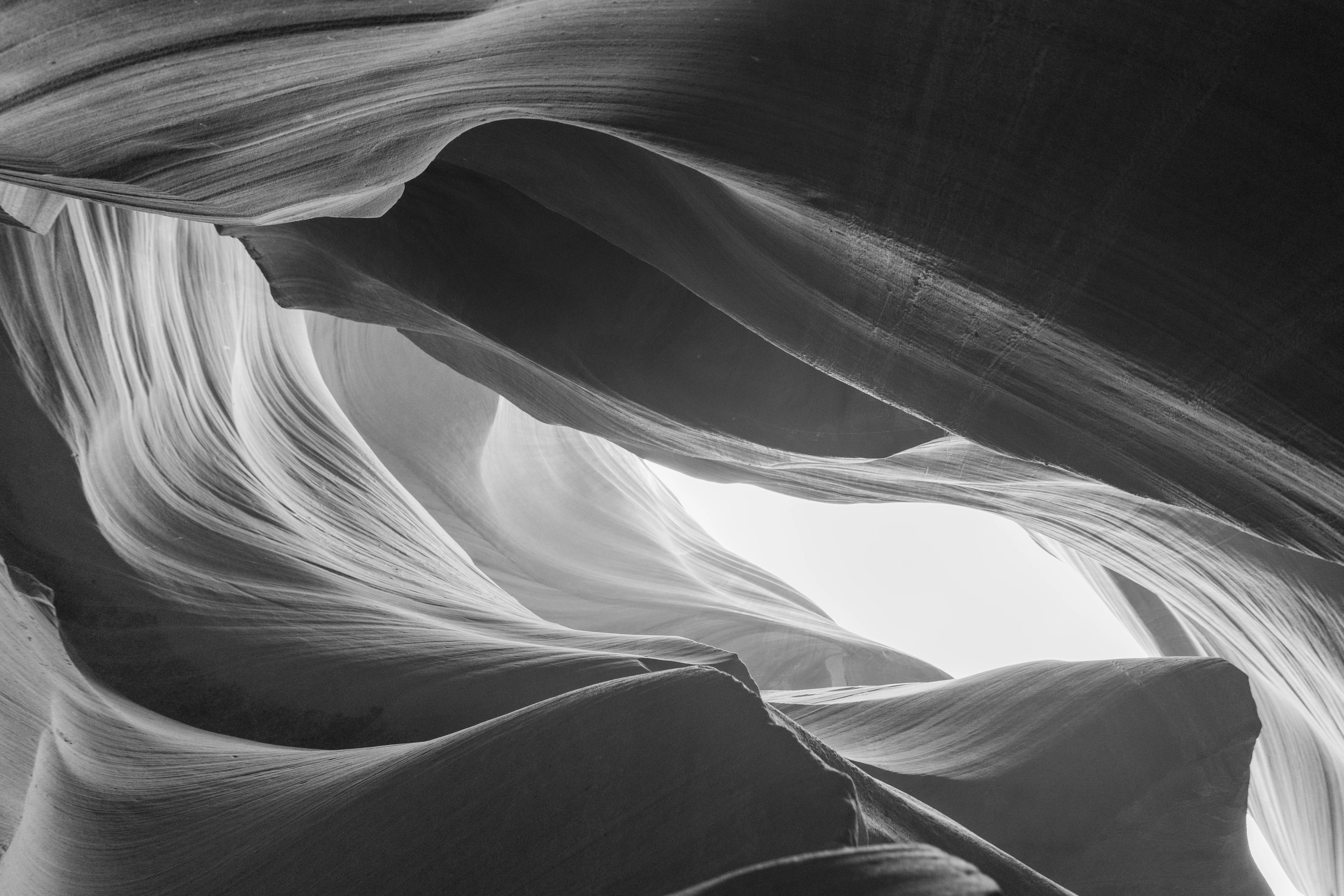 Black-and-white study of the sculpted sandstone walls of Antelope Canyon with light glowing through the gap above