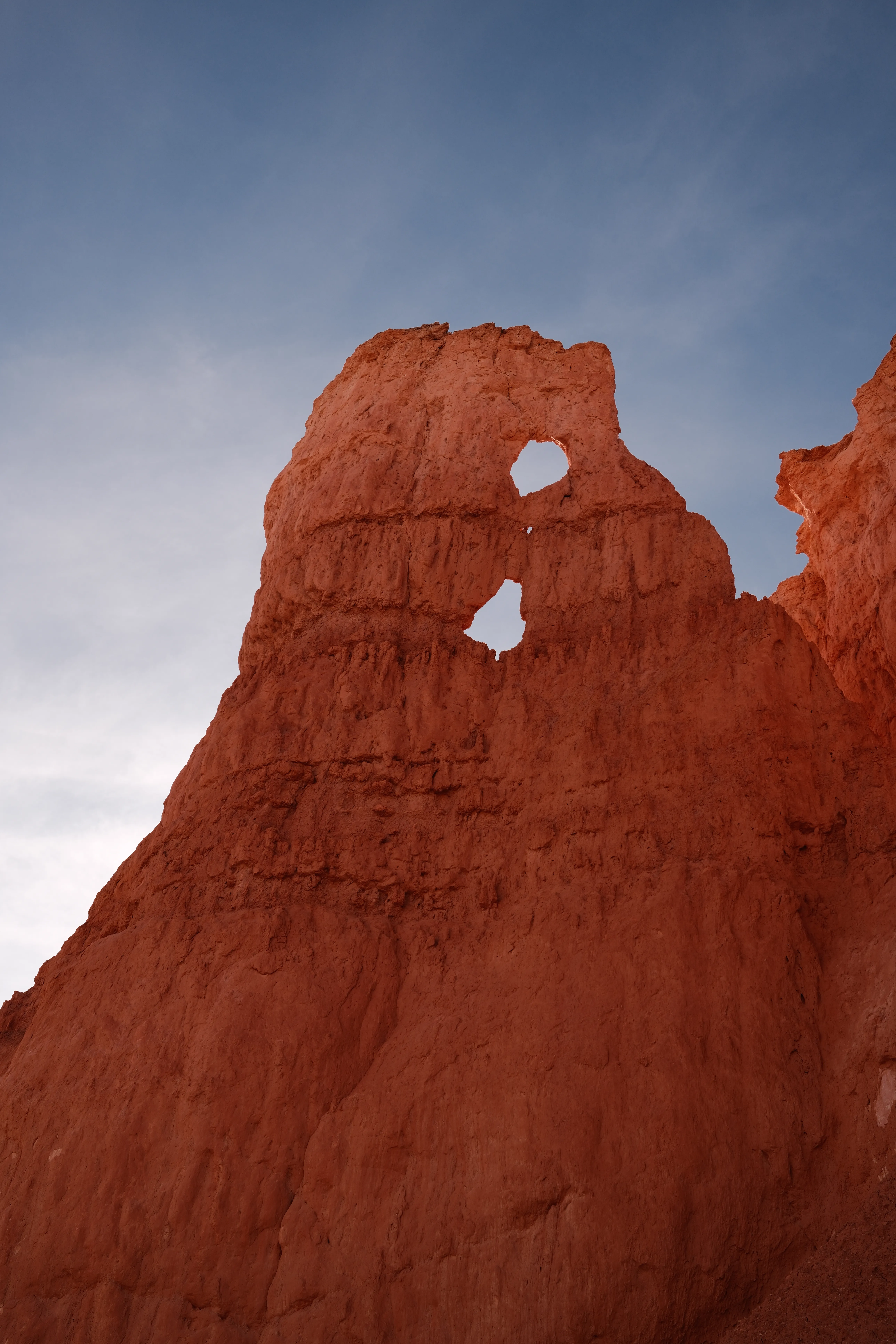 A red-orange Bryce Canyon rock formation with a window eroded through it against a blue sky