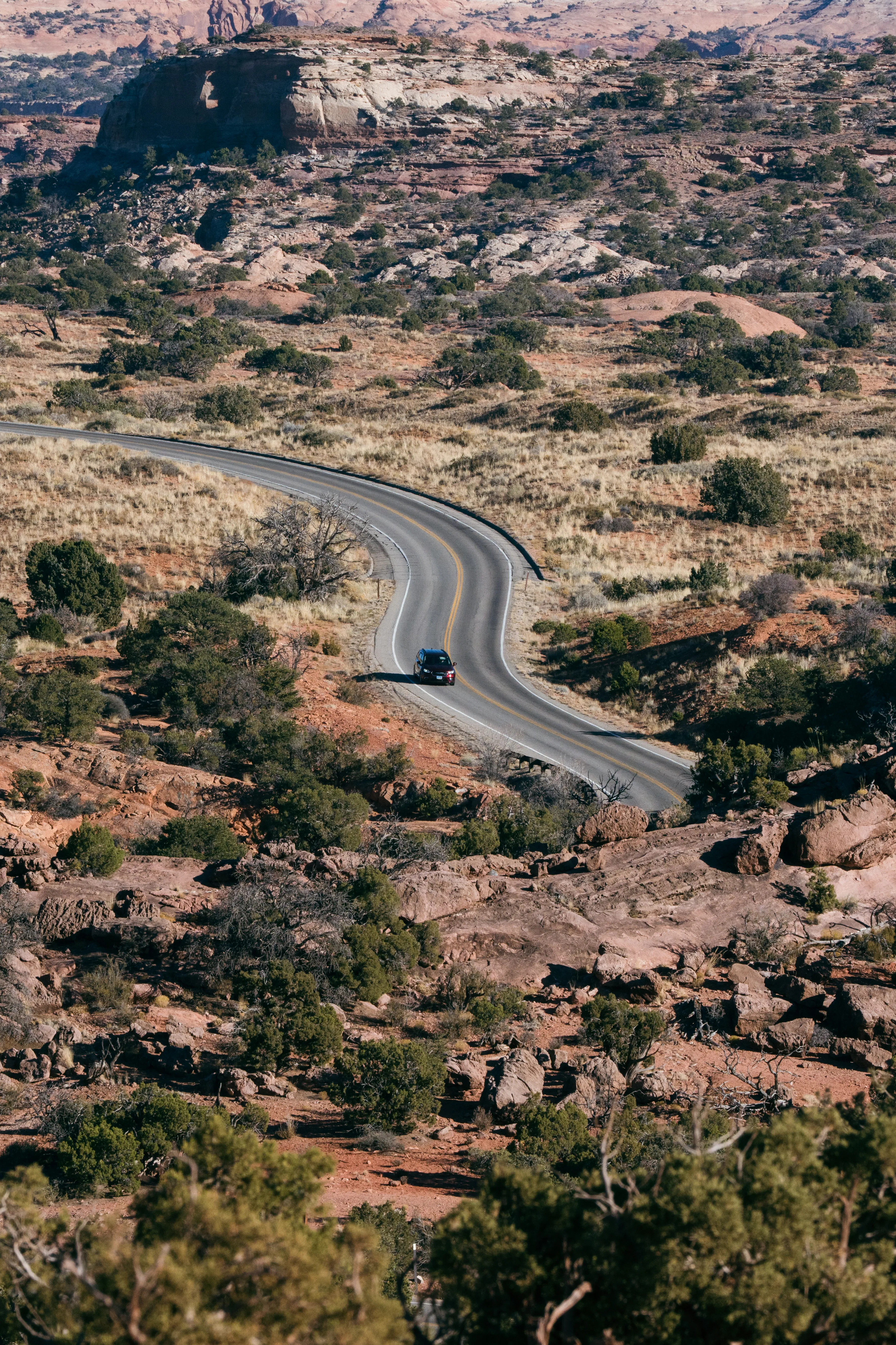A lone car on a winding road cutting through red-rock desert scrub near Canyonlands