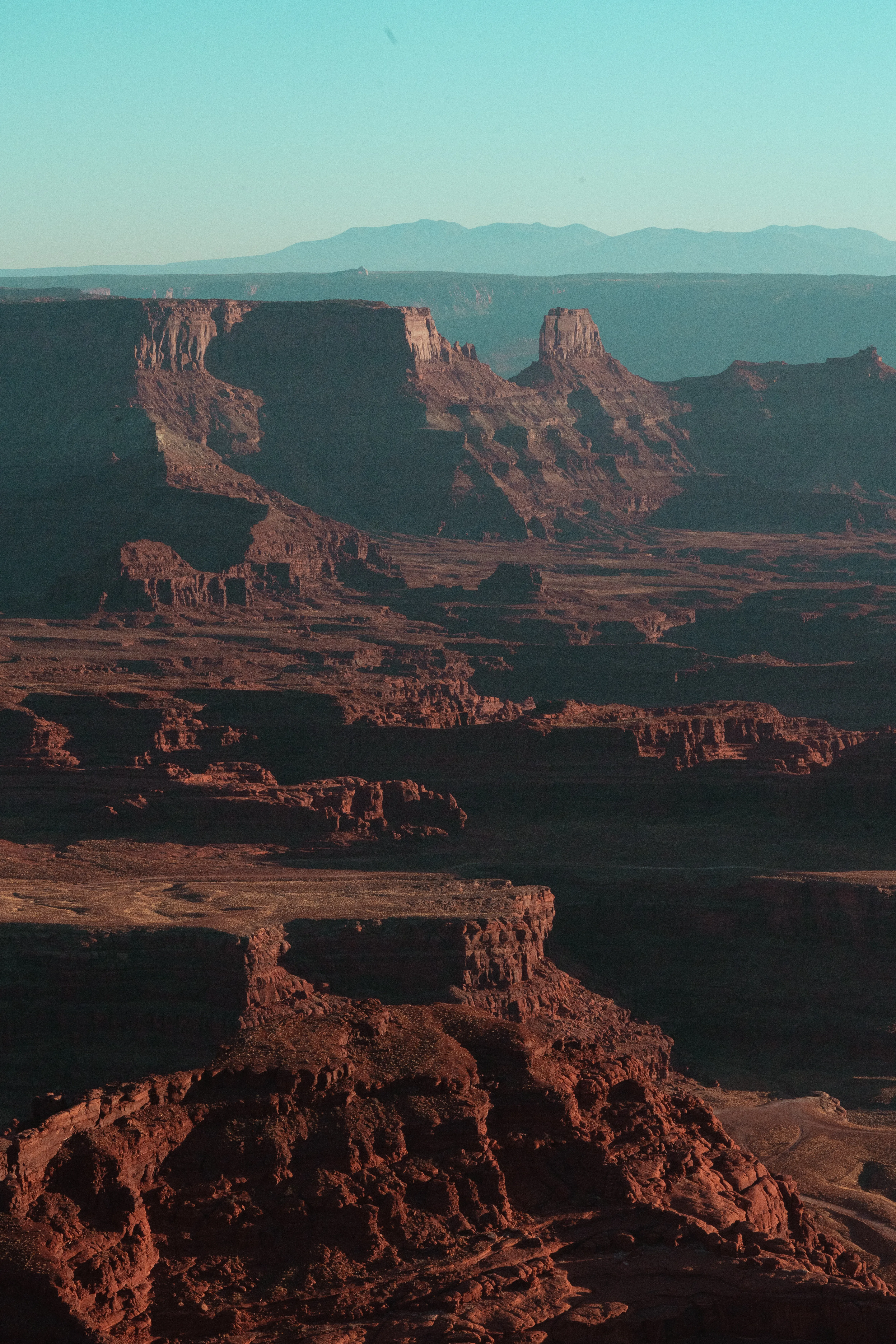 Red-rock mesas and buttes in warm evening light at Dead Horse Point with distant mountains on the horizon