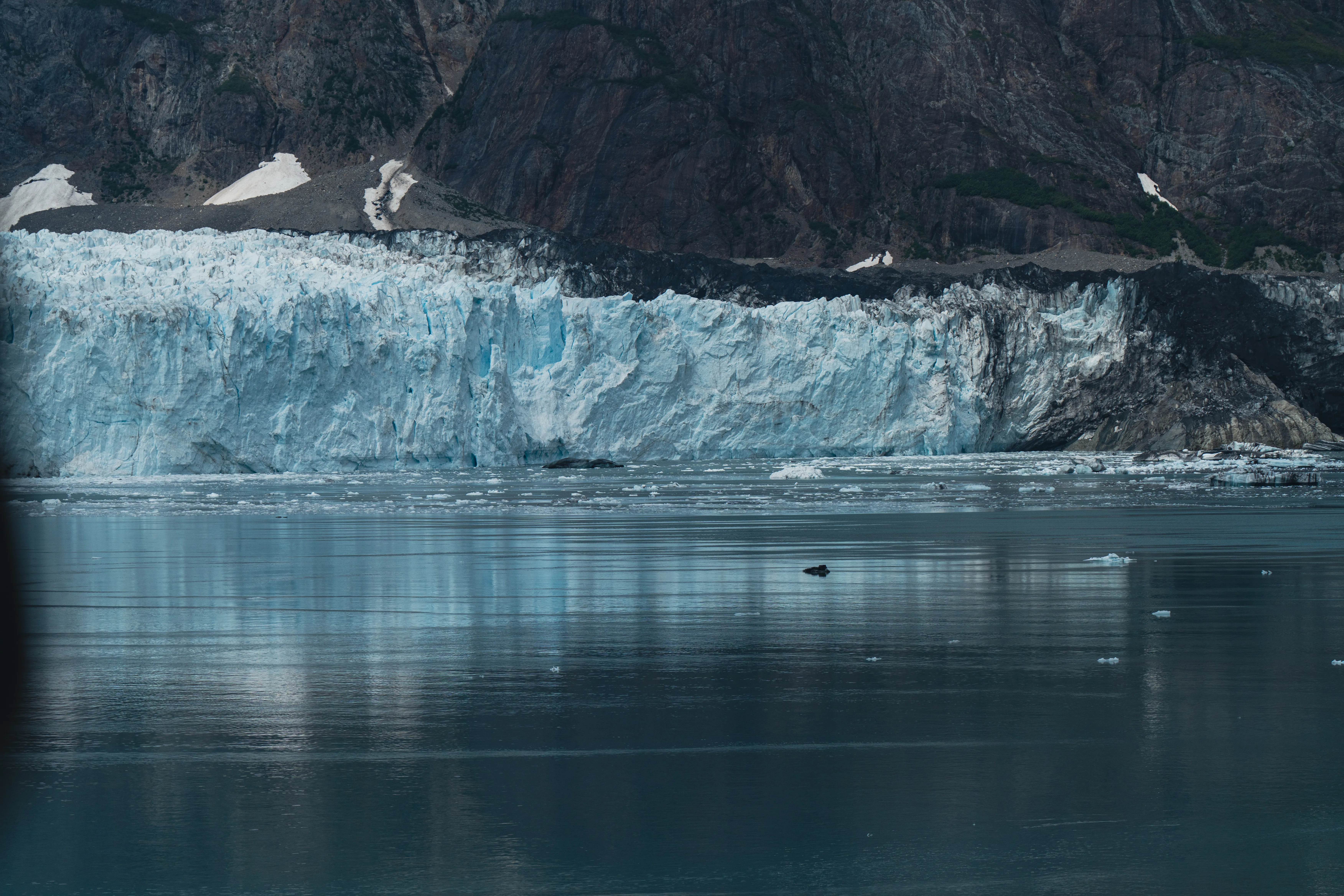 A tidewater glacier's blue face meeting dark rock, mirrored in calm water