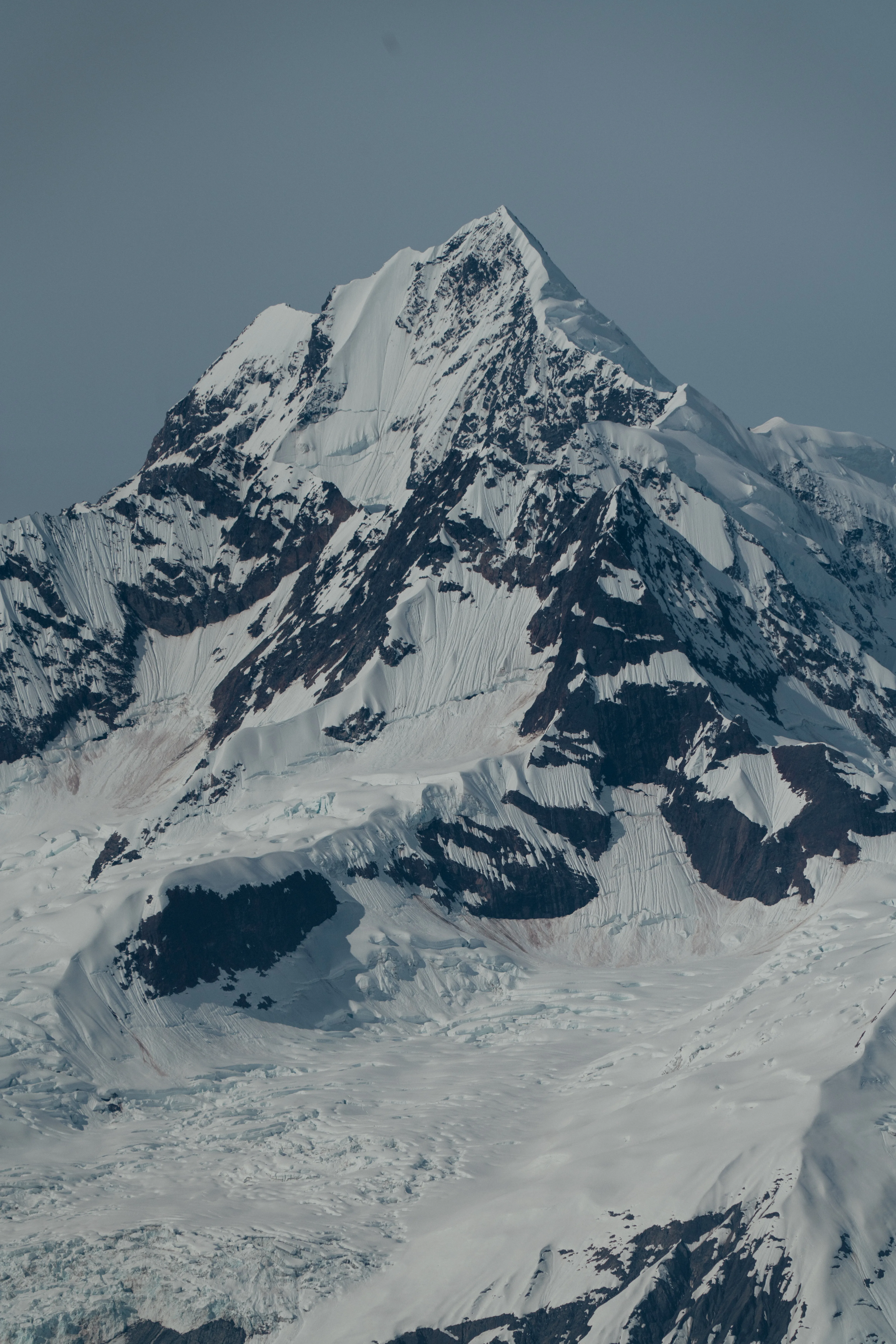 A steep, snow-streaked mountain peak against a clear sky
