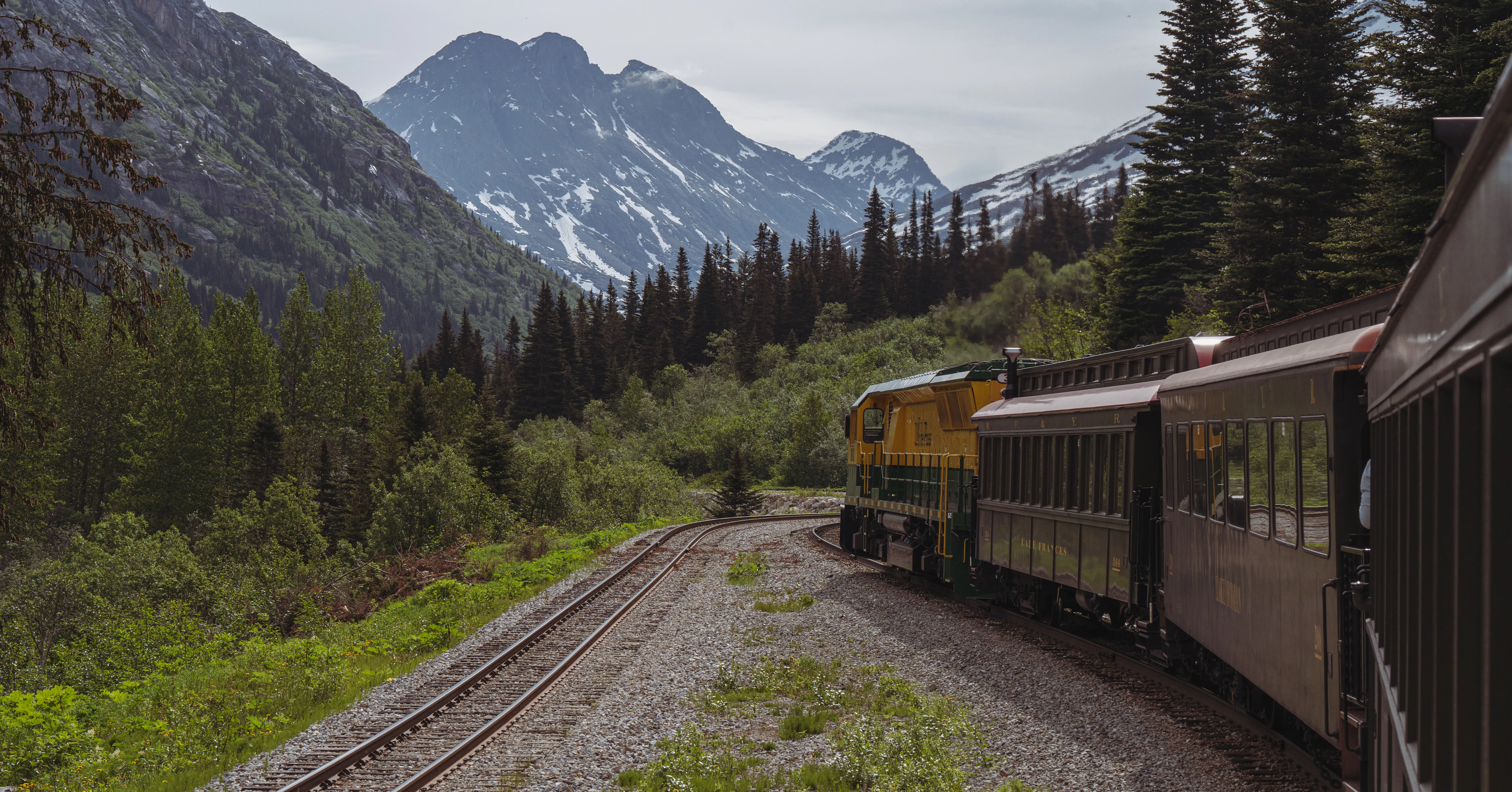 The White Pass railway curving through green forest toward snow-capped peaks near Skagway
